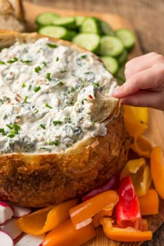 a person dipping dip into a bread bowl filled with vegetables