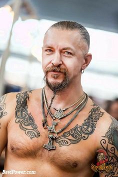 a man with tattoos on his chest wearing a cross necklace and chain around his neck