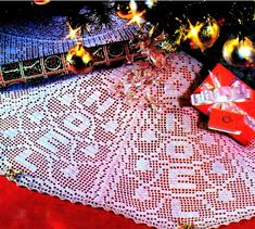 a christmas tree with presents under it on a tablecloth next to a red box