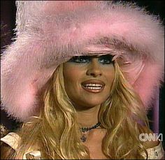 a woman with long blonde hair wearing a pink fur hat and blue eyeshadow