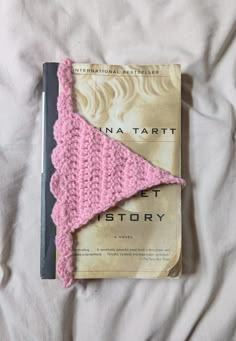 a book with a pink knitted triangle on top of it next to a white sheet