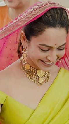 a woman in a yellow sari smiles as she looks down at her cell phone