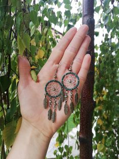 a person's hand holding two earrings in front of some trees and leaves,