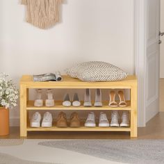 a wooden shoe rack filled with shoes next to a potted plant and wall hanging