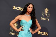 a woman in a blue dress poses on the red carpet at an awards event with her hands on her hips