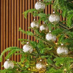 a christmas tree with ornaments hanging from it's branches in front of a wooden wall