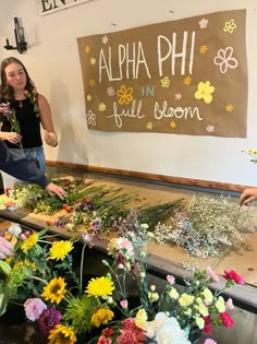 two women are arranging flowers in front of a sign