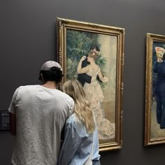 two people looking at paintings on display in a museum