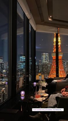 a man sitting on a couch in front of a window with the eiffel tower lit up at night