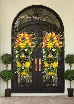 two large wreaths with flowers on them hang from the front door of a house