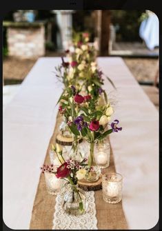 a long table with vases filled with flowers on top of it and candles in the middle