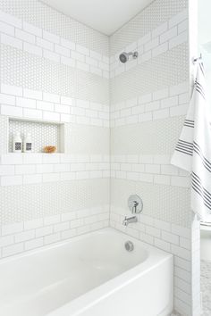 a white tiled bathroom with a tub and shower head