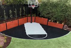 an outdoor basketball court surrounded by grass and bushes with a basketball hoop in the middle