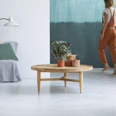 a woman walking past a bed in a room with white walls and flooring,