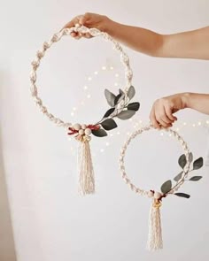 two hands are holding hoop decorations with flowers and leaves hanging from the ends, while another hand is reaching for one