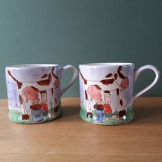 two coffee mugs sitting on top of a wooden table next to each other with cartoon characters painted on them