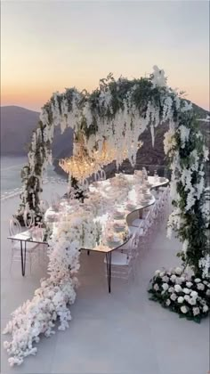 an outdoor dining table with white flowers and greenery on the top is surrounded by chairs