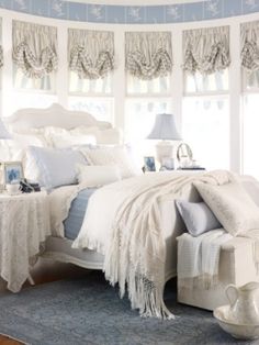 a white bed sitting in a bedroom next to a window covered in blue and white curtains