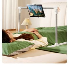 a woman laying in bed under a laptop computer monitor on a desk with a lamp next to her