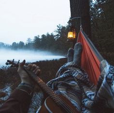 a person laying in a hammock with their feet up and holding a guitar