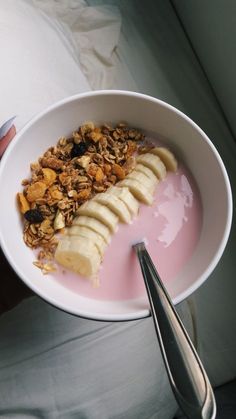 a white bowl filled with granola and sliced banana on top of a pink yogurt