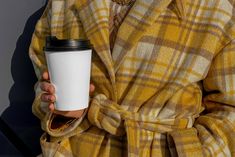 a woman in a yellow coat holding a coffee cup