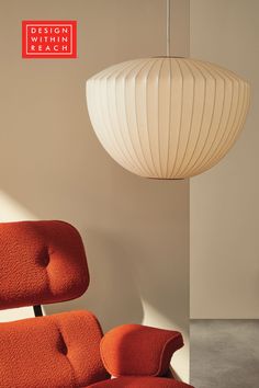 an orange chair sitting in front of a white light hanging from a ceiling fixture above it