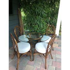 a table with four chairs and a glass top dining set on a brick patio surrounded by greenery