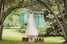 wedding dress hanging on clothes line in front of trees with boots and shoes underneath it