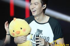 a man holding a yellow stuffed animal in his right hand and singing into a microphone