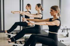 two women in black shirts and leggings are doing exercises on rowing bikes while another woman watches from the side