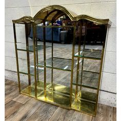 a gold colored glass display case with shelves on the bottom and sides, in front of a white brick wall