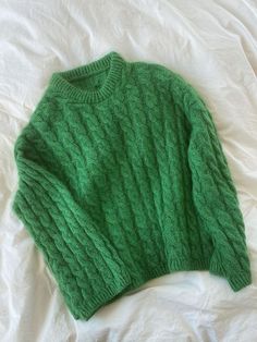 a green sweater laying on top of a bed