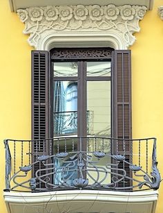 an ornate balcony with wrought iron railings and shutters on the windowsill is seen in front of a yellow building