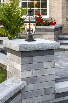 a light on top of a stone pillar in front of a building with flowers and plants