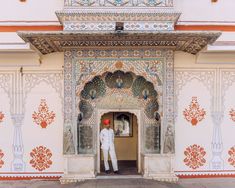 a man in white standing at the entrance to a building with intricately painted walls