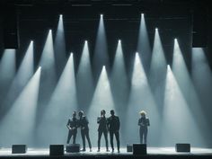 four people standing on stage with spotlights in the background