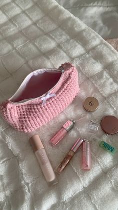 a pink purse sitting on top of a bed next to makeup and other cosmetics items