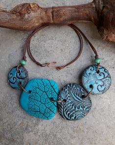 three necklaces with different designs on them sitting on a stone floor next to a tree branch