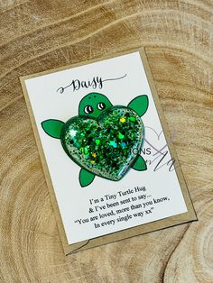 a green heart shaped brooch sitting on top of a piece of wood next to a card