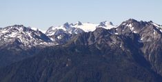 the mountains are covered in snow and green trees