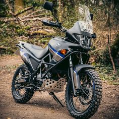 a motorcycle parked on the side of a dirt road in front of some bushes and trees