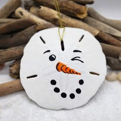 a white snowman ornament with a carrot in it's mouth sitting next to driftwood