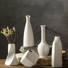 several white vases sitting on top of a wooden table next to rocks and flowers