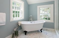 a white bath tub sitting under two windows in a bathroom