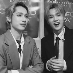 two young men standing next to each other in front of a wall with posters on it