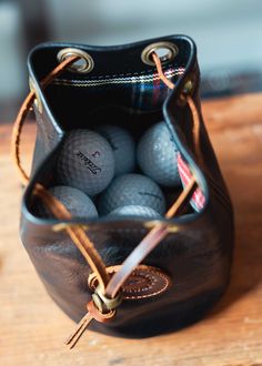 a leather bag filled with golf balls on top of a wooden table