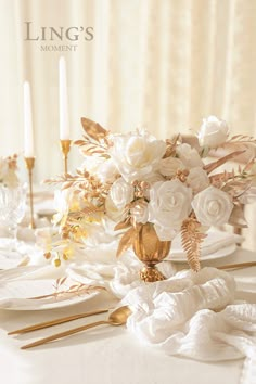 the table is set with white flowers and gold place settings