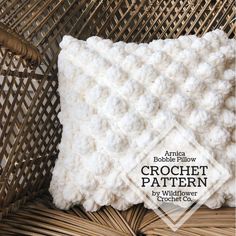 the crochet pillow is made with white yarn and sits on a wicker chair