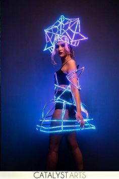 a woman is standing in front of a blue background wearing a light up dress and boots